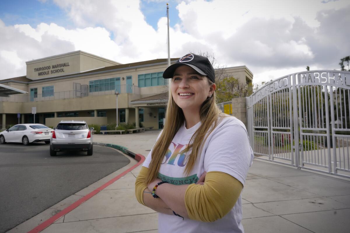 A woman wearing a Scripps Ranch Pride Council T-shirt stands outside a middle school on a cloudy day.