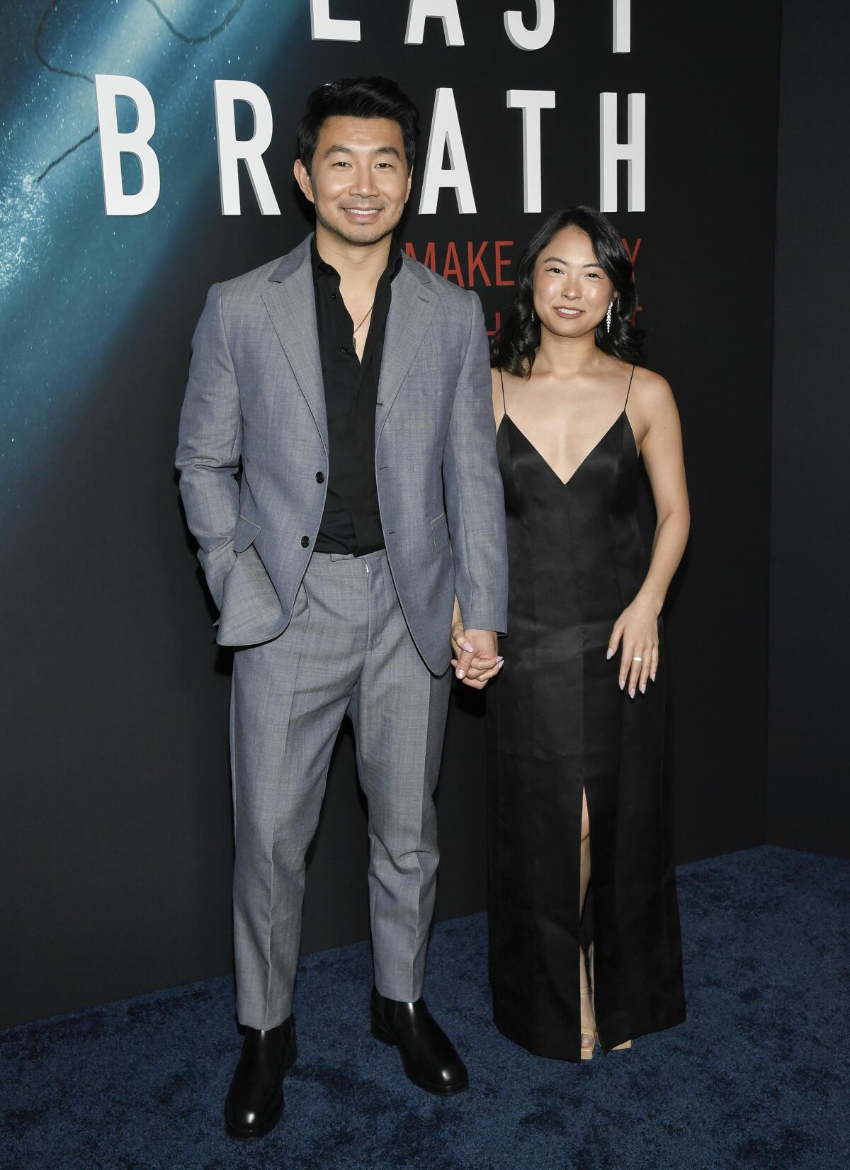 Actor Simu Liu in a gray suit holds hands upon arrival at a movie premiere with girlfriend Allison Hsu