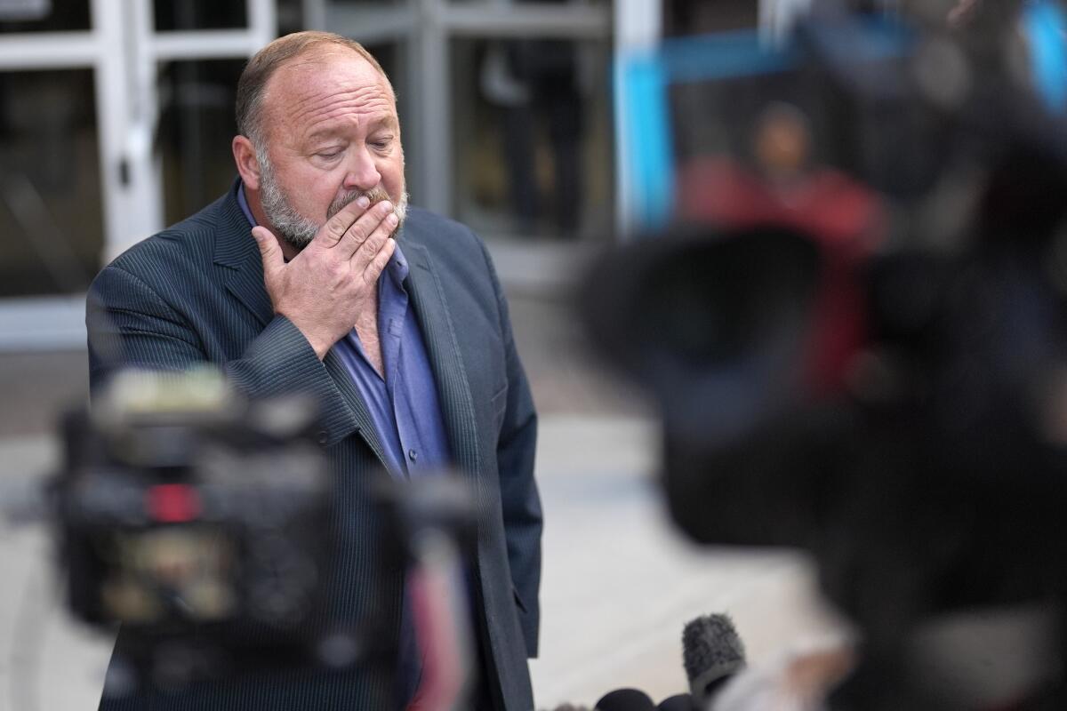 Right-wing conspiracy theorist Alex Jones stands near the news media outside a courthouse.