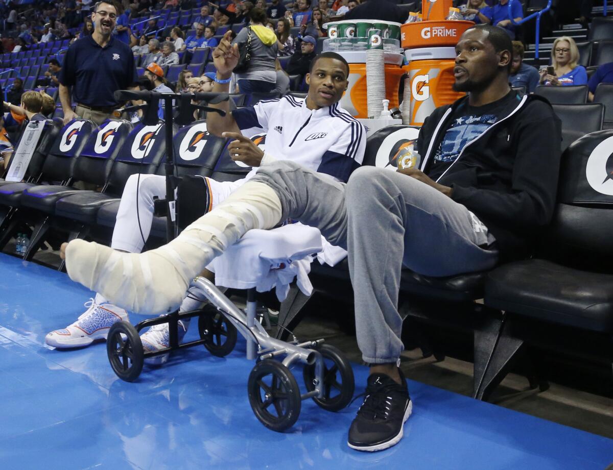 Oklahoma City Thunder guard Russell Westbrook, left, talks with teammate Kevin Durant, who's recovering from a broken bone in his foot, before the start of a preseason game against the Utah Jazz on Oct. 21.