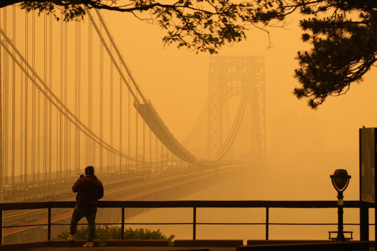 A man talks on his phone as he looks through the haze at the George Washington Bridge from Fort Lee, N.J.