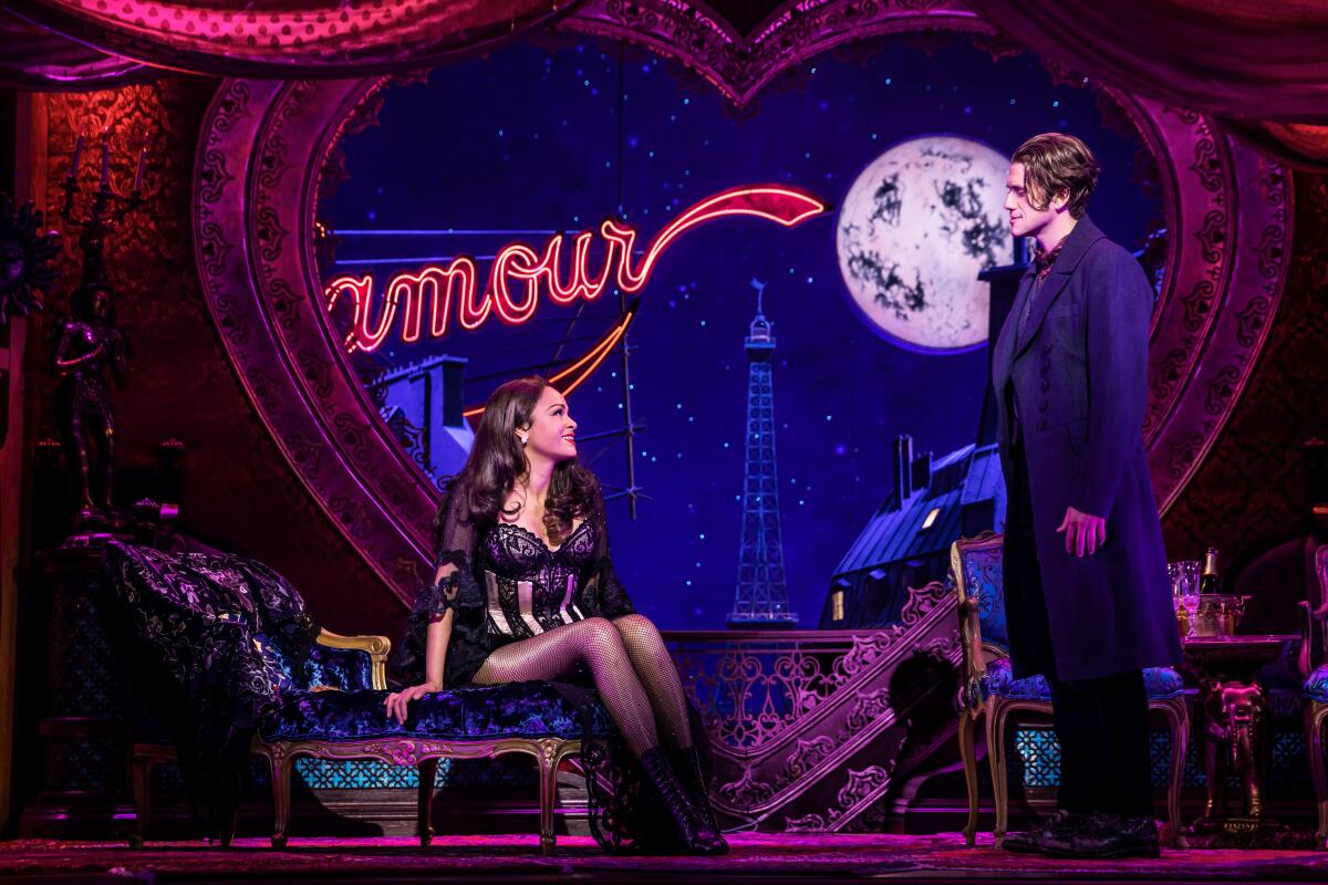 Karen Olivo and Aaron Tveit in a scene from "Moulin Rouge!" with a "L'Amour" sign and a full moon in the background.