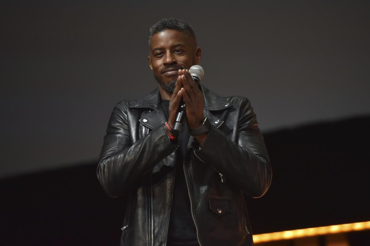 A man in a leather jacket claps his hands while holding a microphone