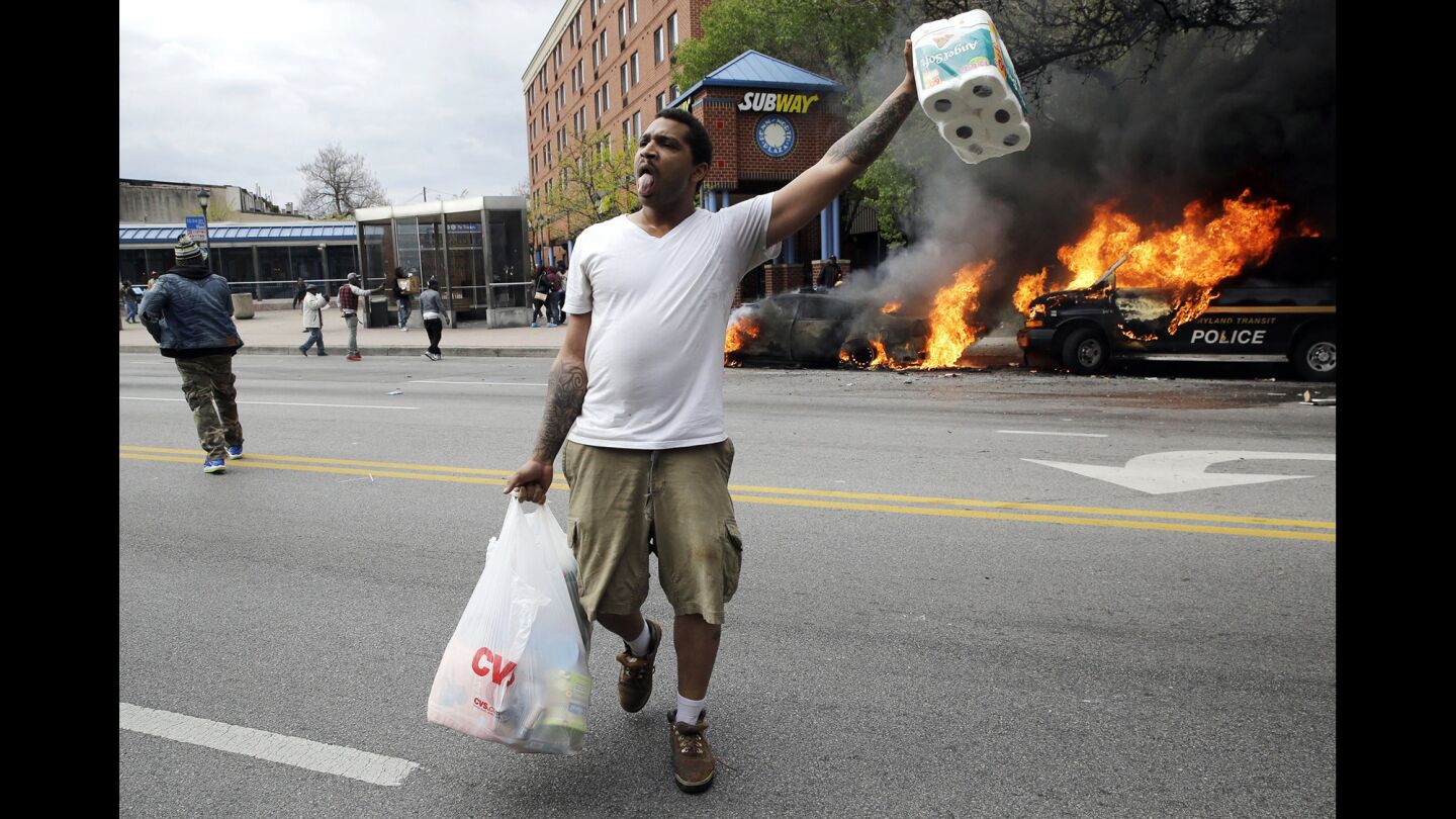 A man carries items from a store as police vehicles burn after the funeral of Freddie Gray in Baltimore on Monday.