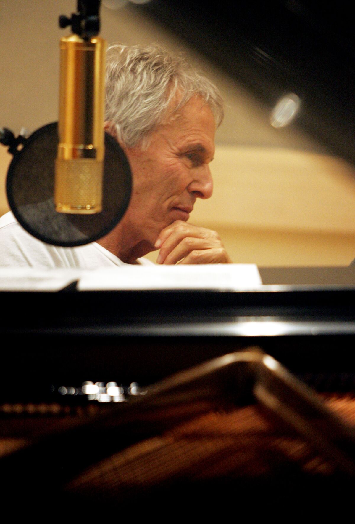 A man listens while sitting in a studio by a piano