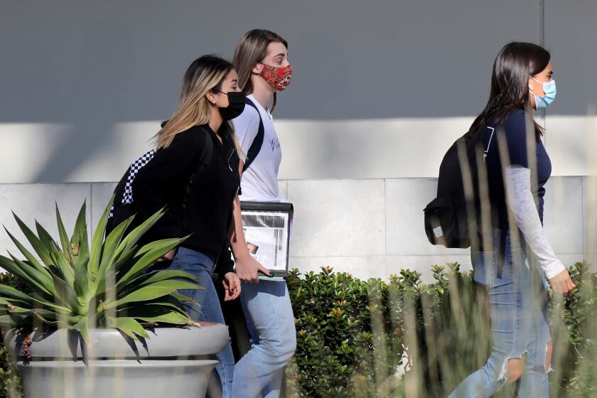 Students wear facial masks on the 1100 block of Irvine Ave., as they walk towards a row of restaurants, in Newport Beach on Friday, Nov. 13, 2020.