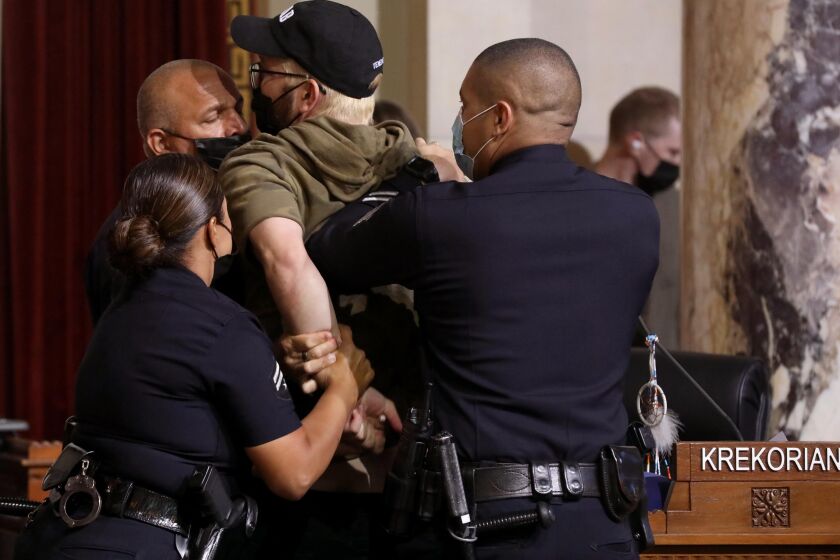 LOS ANGELES, CA - AUGUST 8, 2022 - - Ricci Sergienko, with The People's City Council, is arrested by police officers after crossing a police line in city council chambers at City Hall in Los Angeles on August 8, 2022. Homeless advocates and protesters shut down proceedings in the Los Angeles City Council chambers who had to stop from casting their final vote on a law prohibiting homeless encampments near schools and daycare centers at City Hall on August 8, 2022. Members of the LAPD created a defense line as city council members left chambers. Protesters left the chambers after being threatened with arrest. Two arrests were made during proceedings. (Genaro Molina / Los Angeles Times)