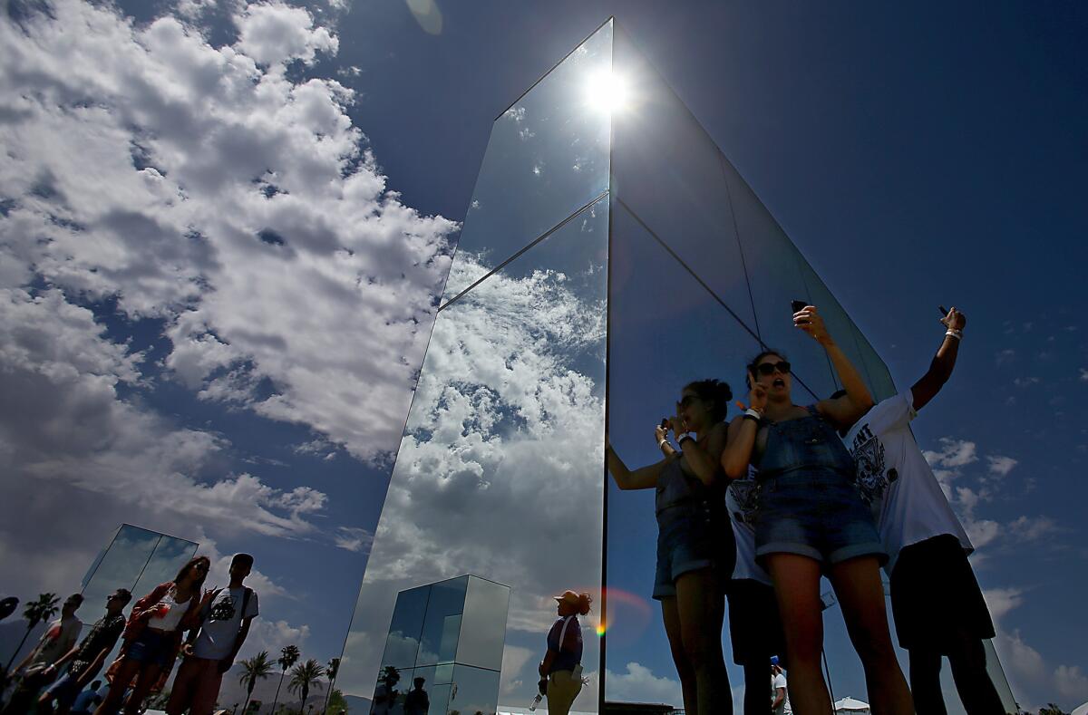 The sun reflects brightly on mirrored works of art as the gates open and participants take phone camera selfies on the first day of the Coachella Valley Music and Arts Festival on Friday.