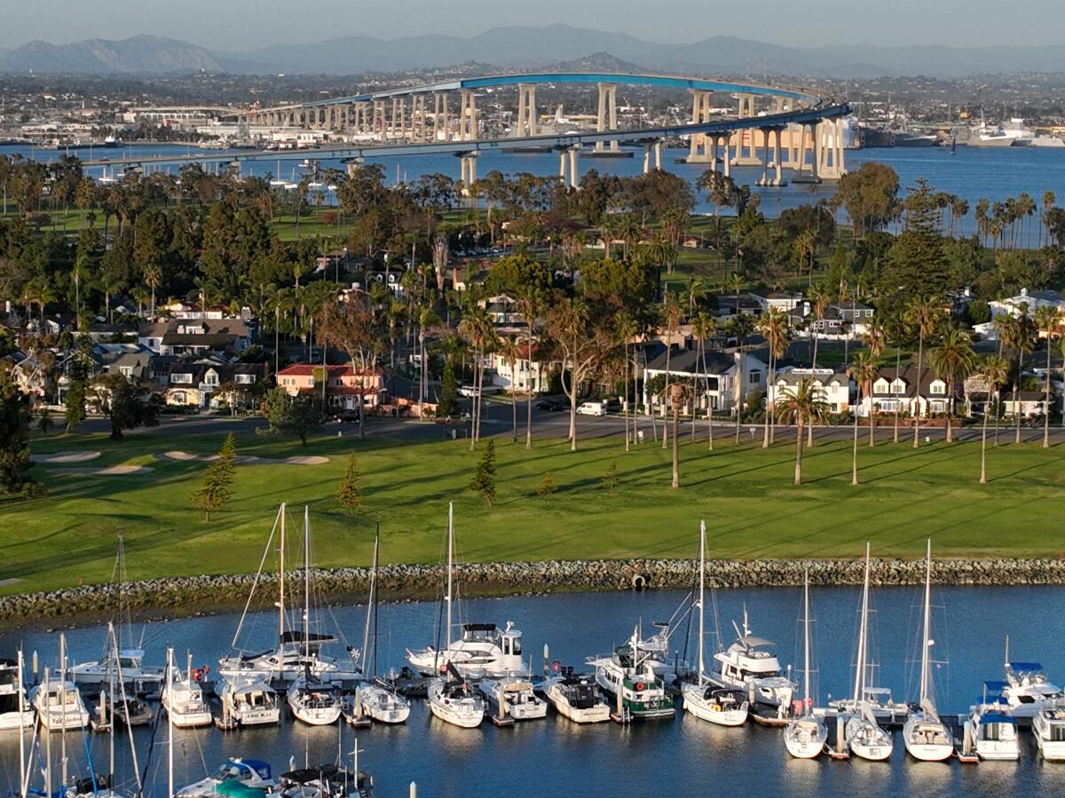 A bridge in the distance with homes, a green golf course and boats in a marina in the foreground.