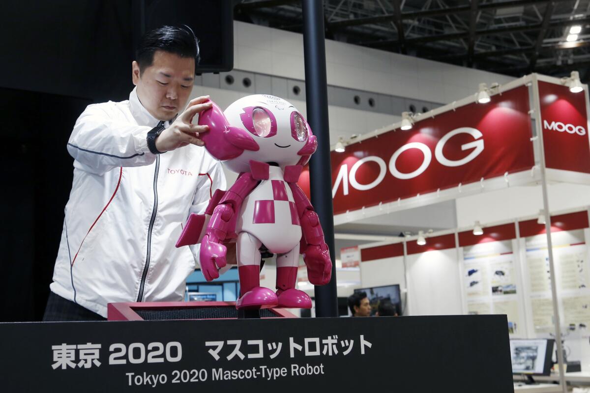 A man places a small anthropomorphic robot on a table.