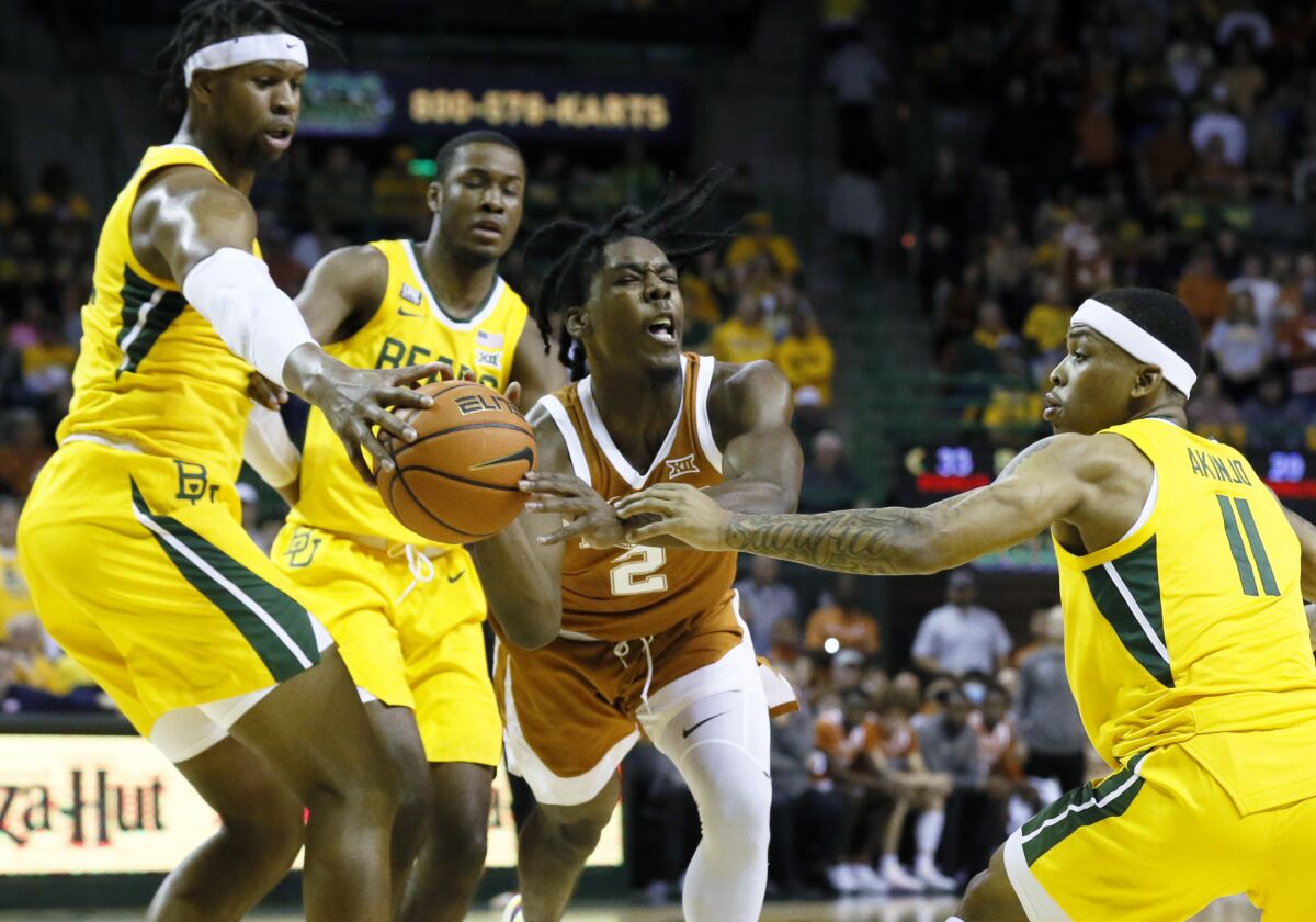 Texas guard Marcus Carr, center, turns over the ball as he is defended by Baylor forward Flo Thamba, left and Baylor guard James Akinjo, right during the first half of an NCAA college basketball game on Saturday, Feb. 12, 2022, in Waco, Texas. (AP Photo/Ray Carlin)