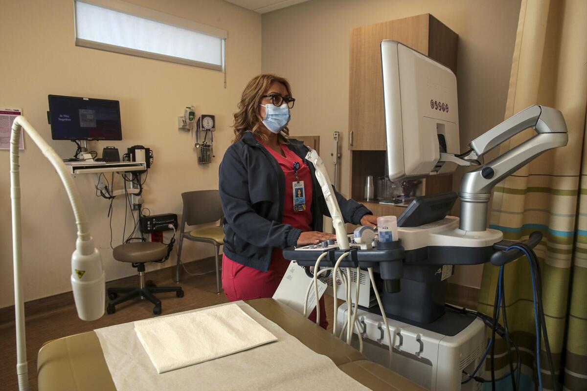 A woman in a mask and scrubs looks at a computer screen inside a treatment room.