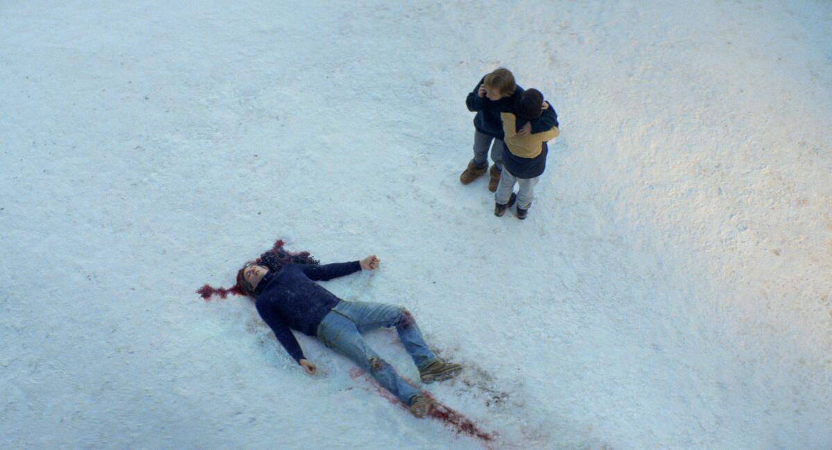 A mother and son look at a man's dead body in the snow in a scene from "Anatomy of a Fall."