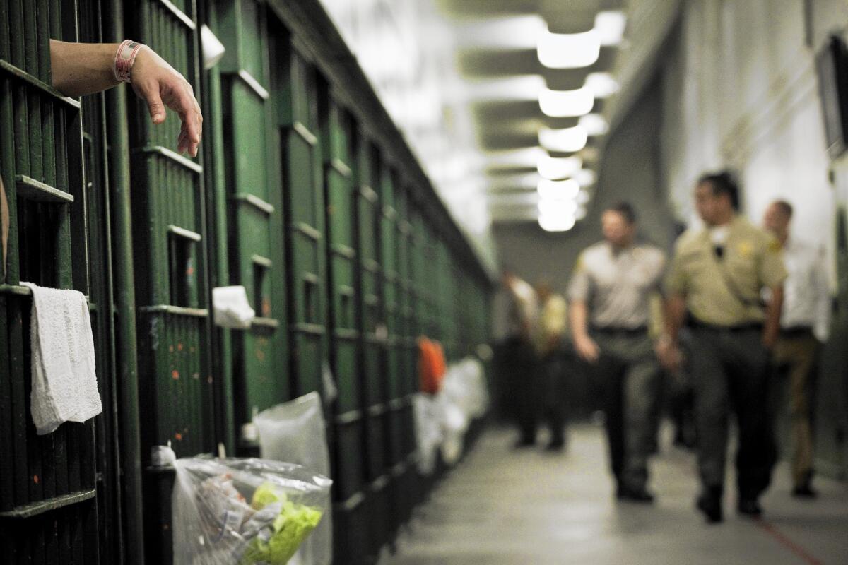 An inmate drapes his hand through the bars of his cell on the 3000 floor of L.A. County Men's Central Jail as sheriff's deputies patrol.