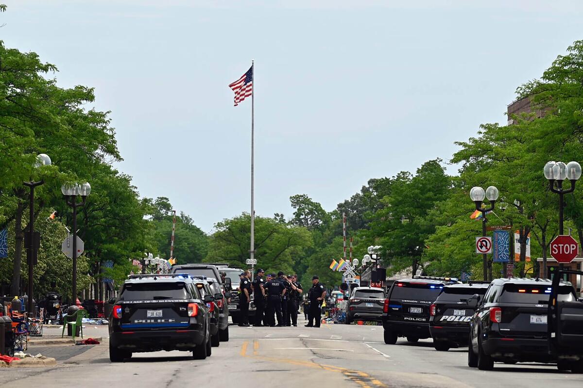 Police officers and vehicles stand in the street below a U.S. flag.