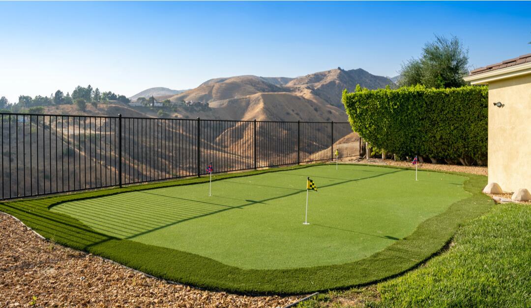 A metal fence borders a putting green with a view of hills.