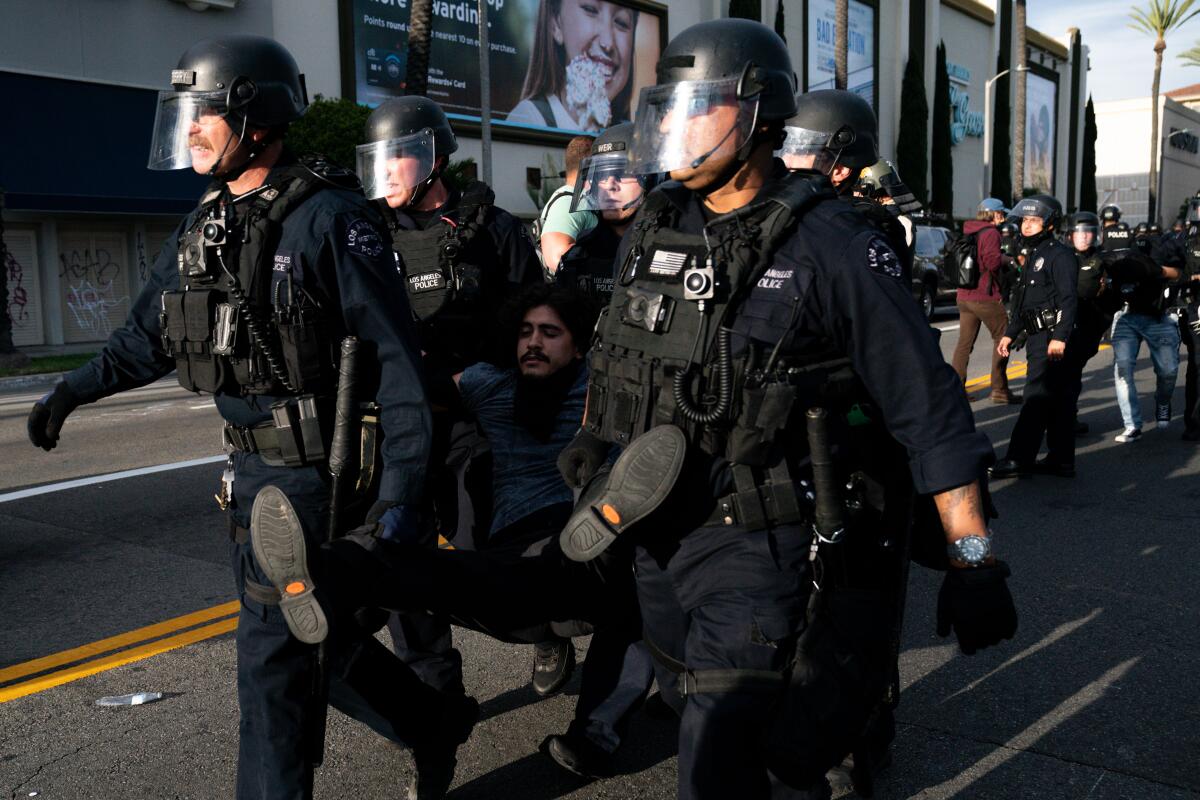 Police in heavy protective equipment carry a man away in the Fairfax District on May 30