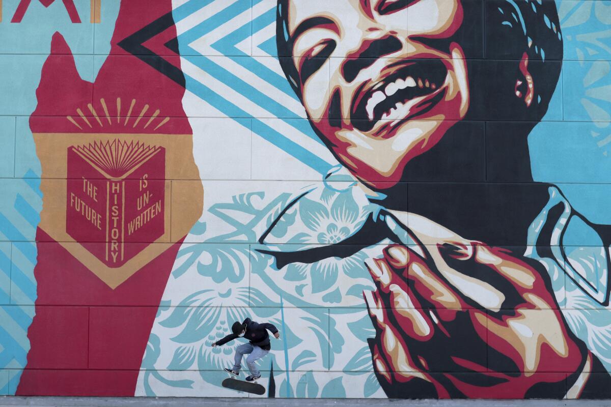 A skateboarder passes a mural depicting Maya Angelou.