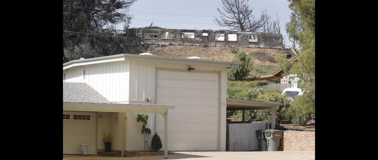 A home on Olive View Road looks untouched while a home on the street overlooking Olive View Road is a total loss in the West Fire.
