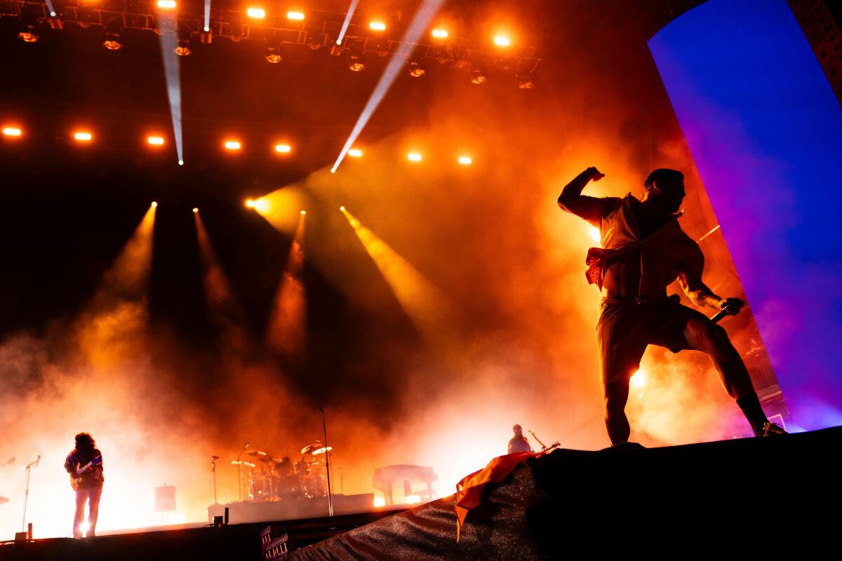 Músicos en el escenario contra espectaculares luces rojas y doradas.