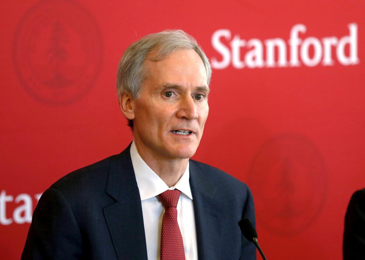 A head-and-shoulders horizontal frame of a man in suit and red tie in front of a red background with "Stanford" writting