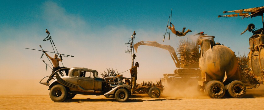 A man holds a spear atop a moving car while another takes a flying leap in a scene from "Mad Max: Fury Road"