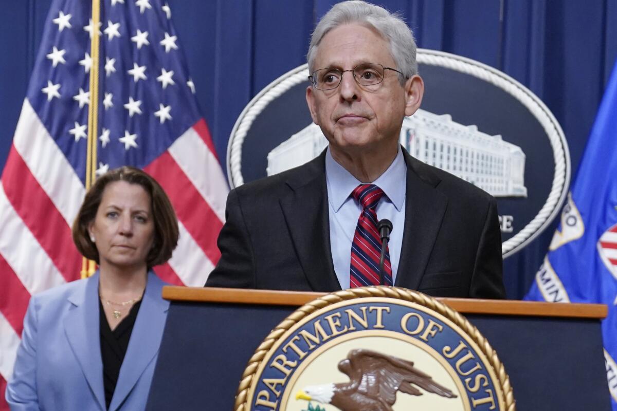 A man at a Department of Justice lectern and a woman in a blue jacket in the background 