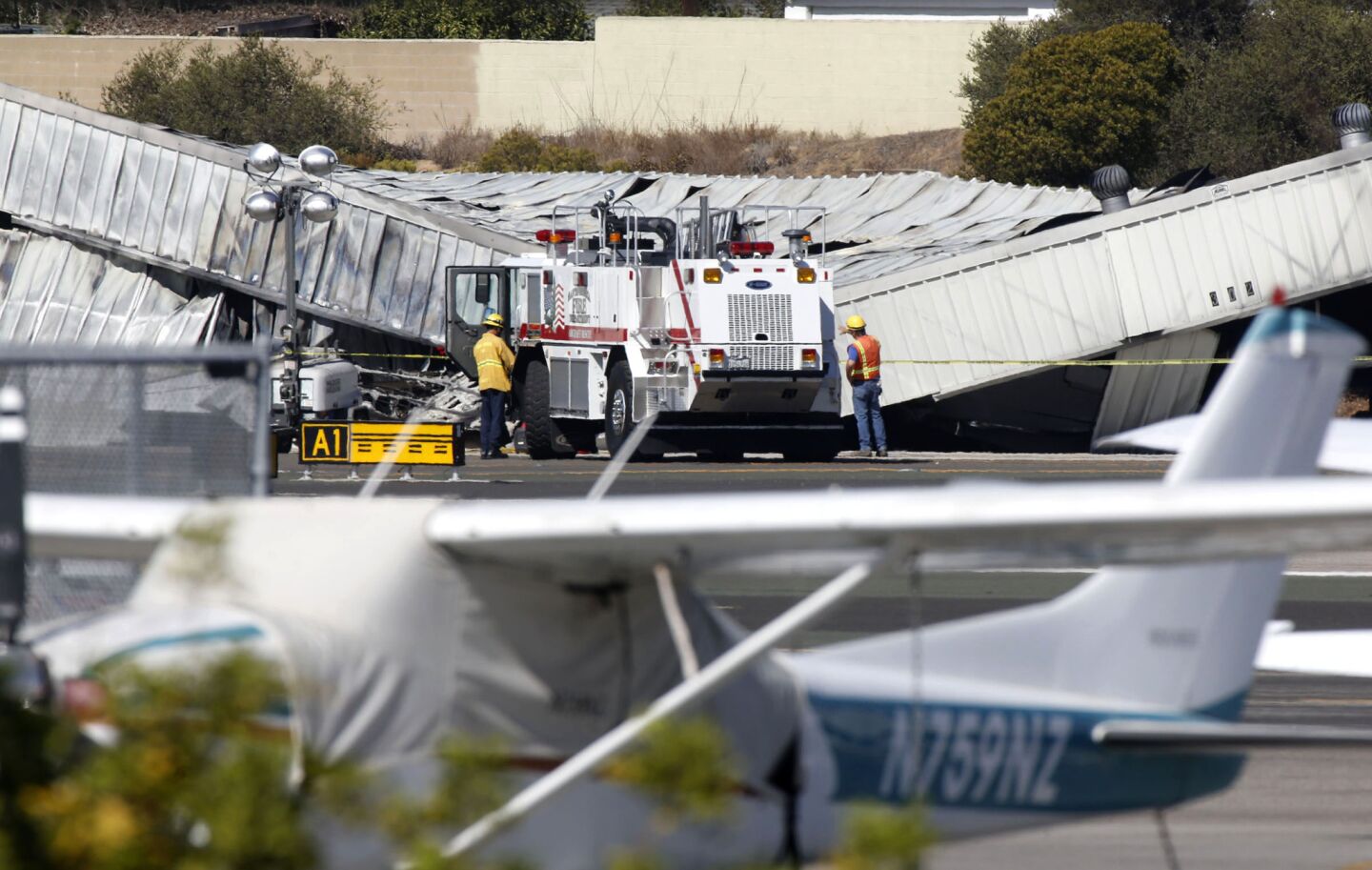 Santa Monica firefighters monitor the collapsed aircraft hangar where a private jet crashed and burned Sunday evening at Santa Monica Airport. Investigators will have to lift the hangar's metal roof off the burned aircraft to determine how many bodies are inside.