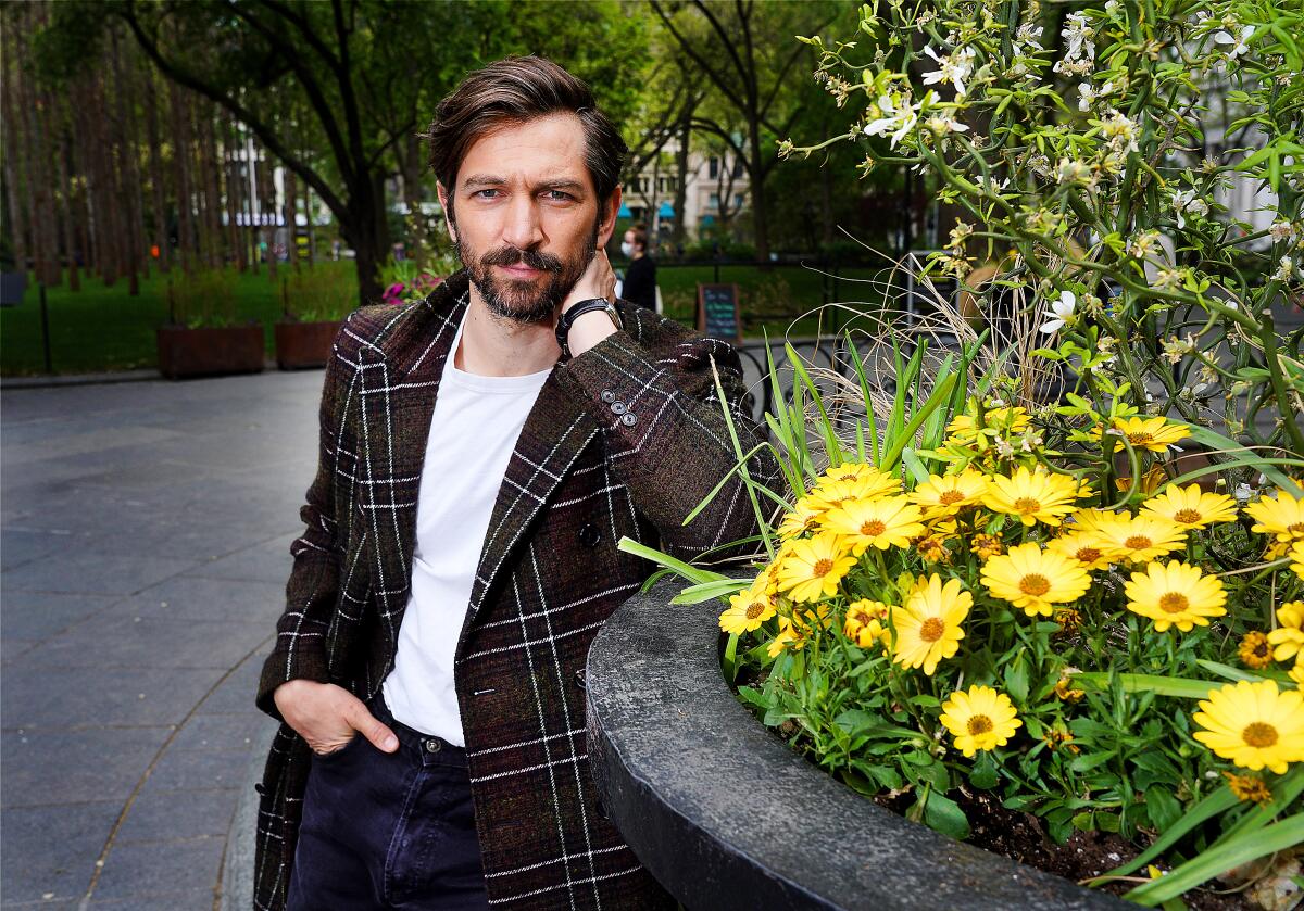 Michiel Huisman ("The Flight Attendant") leans against a pot brimming with yellow African daisies.