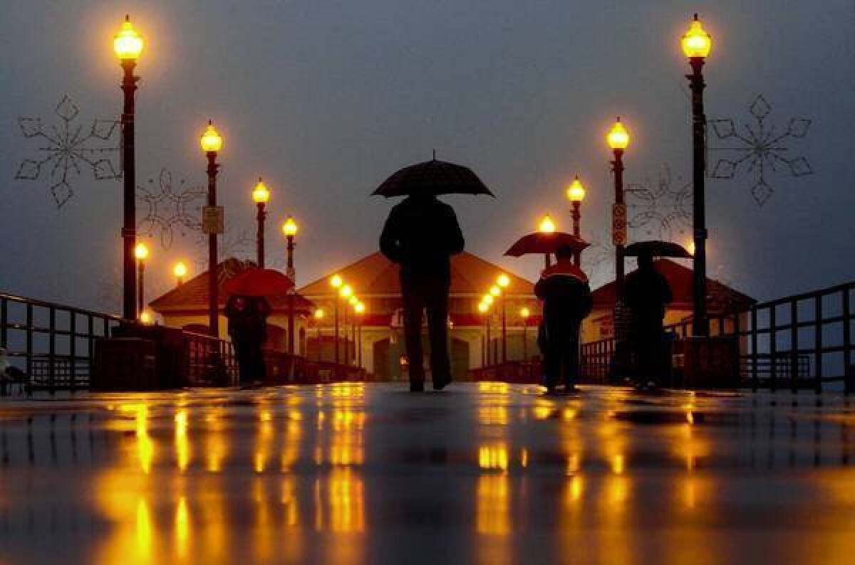 Far removed from the many SigAlerts and traffic accidents caused by the rain, umbrella-toting pedestrians stroll on the Huntington Beach Pier before dawn on Thursday.