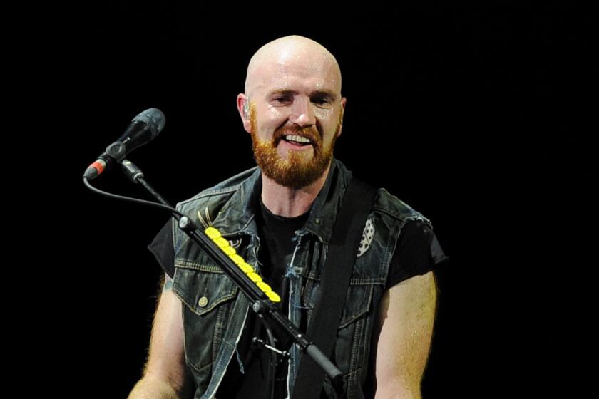 Mark Sheehan of The Script in a sleeveless leather vest holding a guitar on a stage