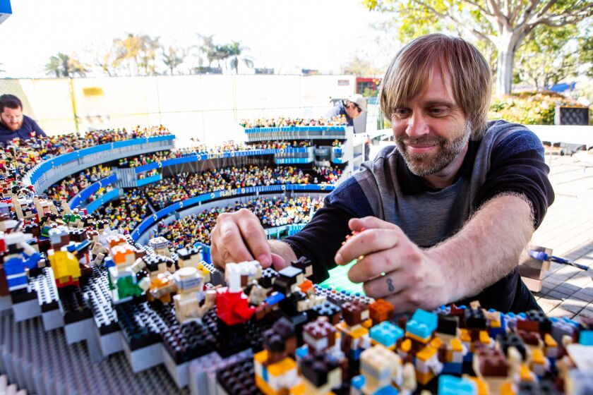 A man works on Lego model of SoFi Stadium for a theme park. 