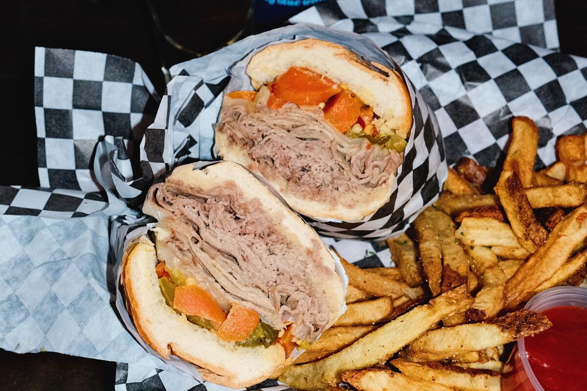 A vertical photo of an Italian beef sandwich and fries with a Hamm's beer and a shot of Jeppson's Mal?rt at The Escondite bar