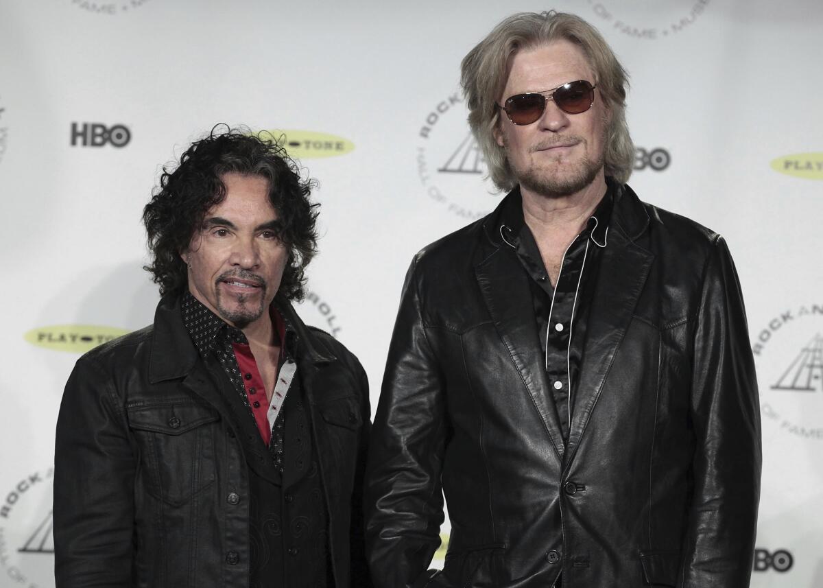  John Oates standing with Daryl Hall, both wearing black jackets