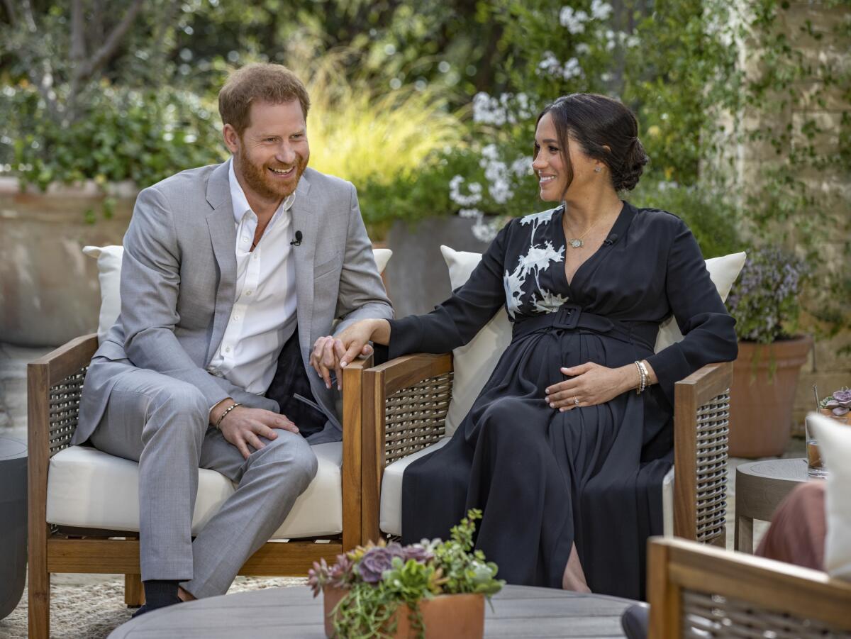 Prince Harry holds wife Meghan's hand as the two sit outdoors