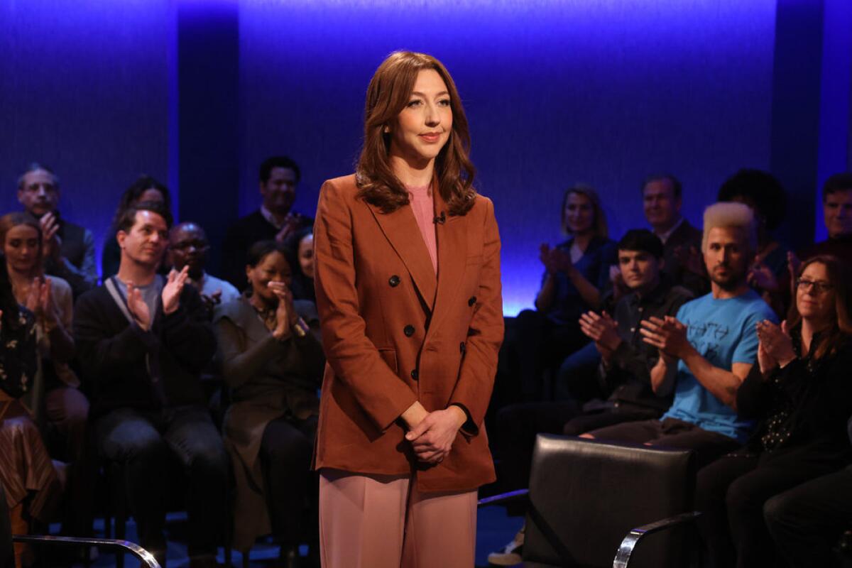 Heidi Gardner stands on the 'SNL' stage in a chestnut blazer.