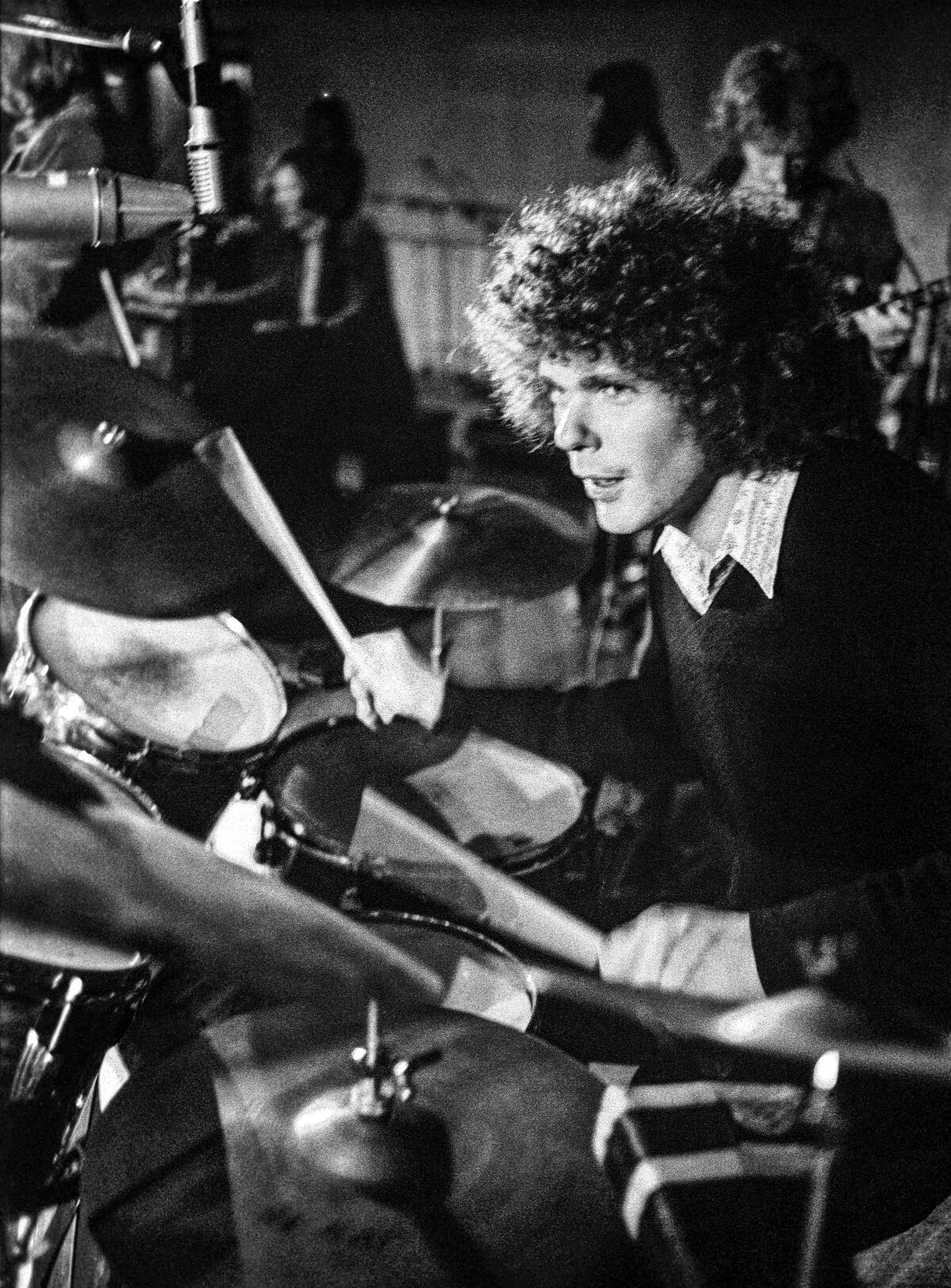 A black-and-white photo of Jim Gordon, with curly hair, playing drums.