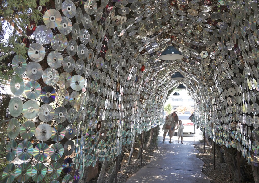 A mother and daughter look down a tunnel cut through brush and covered with music CDs at the LAB Anti-Mall in Costa Mesa.