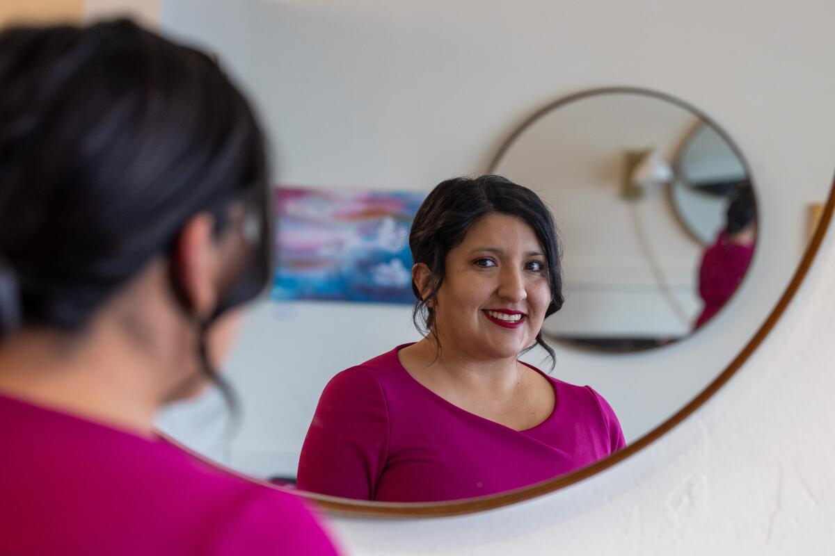 Le reflet de la sénatrice d'État Melissa Hurtado regardant la caméra alors qu'elle fait face à un grand miroir rond