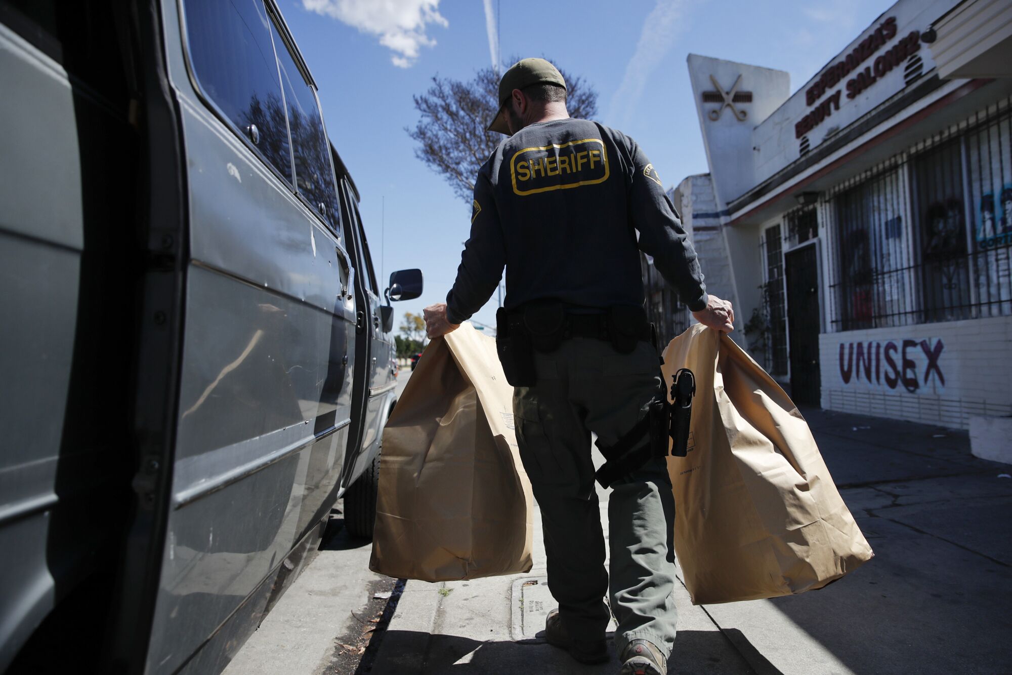 A sheriff's deputy carries two large brown bags