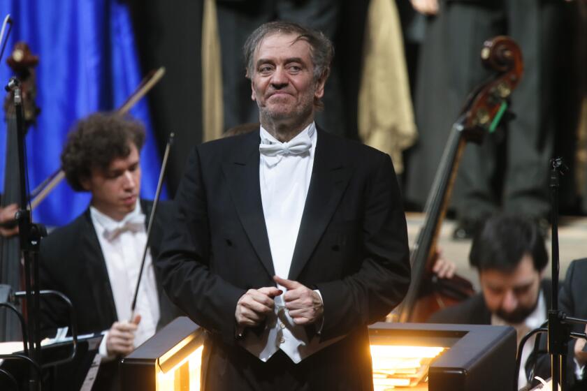 A music conductor wearing a tuxedo leads an orchestra