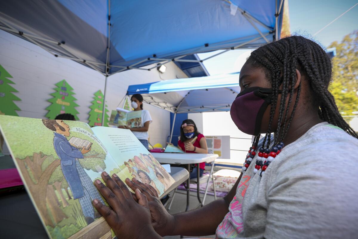  Nyairee Jenkins, right, reads a book in an outdoor class under a canopy at Freedom Schools.