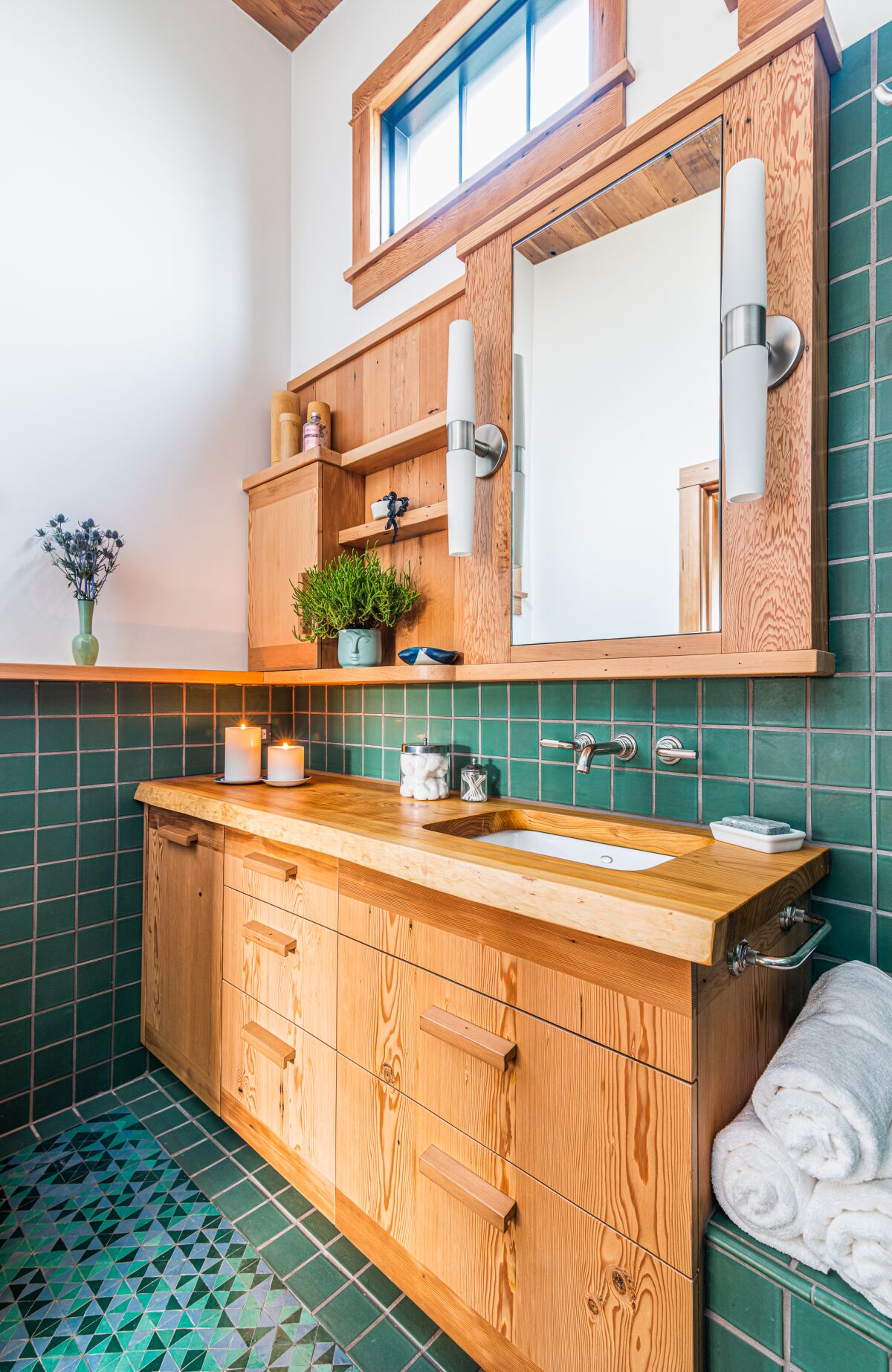 A bathroom with green tile and wood cabinets 