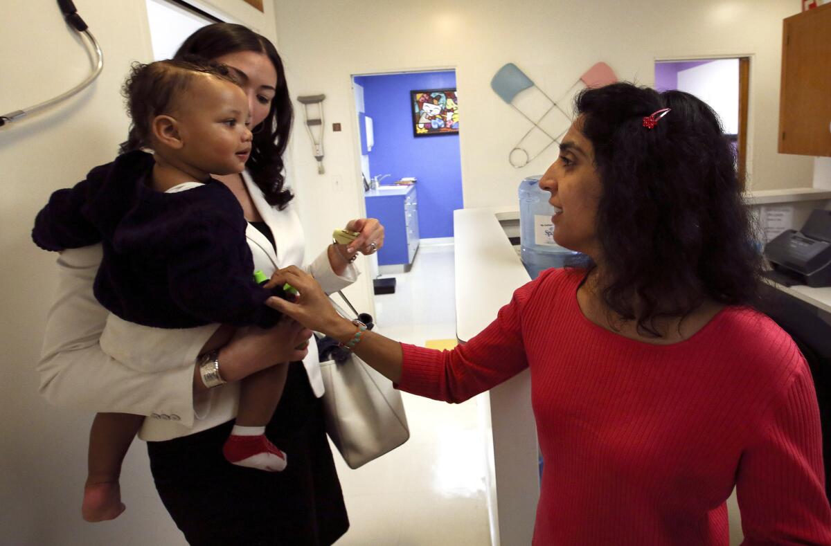 Dr. Monica Asnani, right, says goodbye to Kristian Richard, 1, being held by his mother Natasha, after the child was given a measles-mumps-rubella vaccine at the Medical Arts Pediatric Med Group on Wilshire Boulevard in Los Angeles.