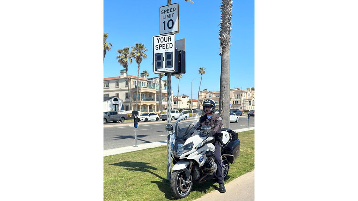 A Huntington Beach Police officer watches next to speed sign along a bike trail.