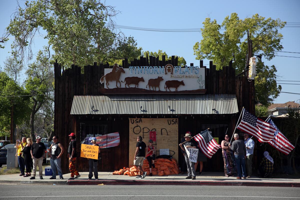 People hold signs and American flags outside a boarded-up restaurant. 
