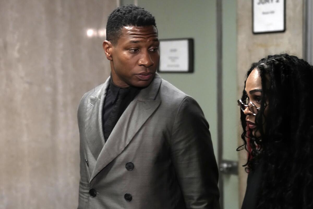 Jonathan Majors leaves a courtroom in a gray suit next to Megan Good who is dressed in black