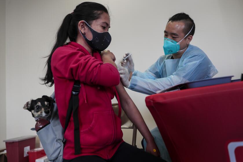 Los Angeles, CA, Monday, April 12, 2021 - Ruth Hancock with Kylie receives a vaccination shot from Medical Assistant Jason Liang at a Covid-19 vaccination site operated by LA County, Chinatown Service Center and CORE in Chinatown. (Robert Gauthier/Los Angeles Times)