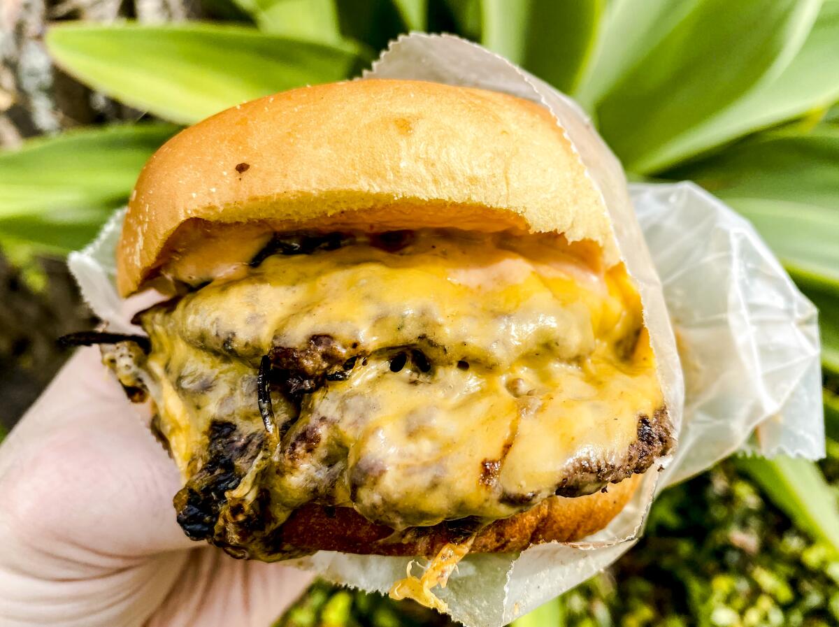 A hand holds a paper-wrapped double cheeseburger.