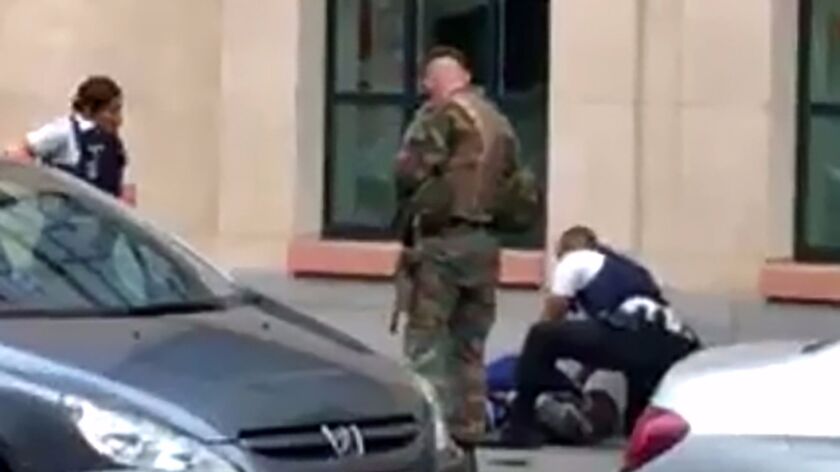 In a screen grab, police officials and a soldier look at a man on the pavement in Brussels, where authorities say a person was shot after attacking troops with a knife.